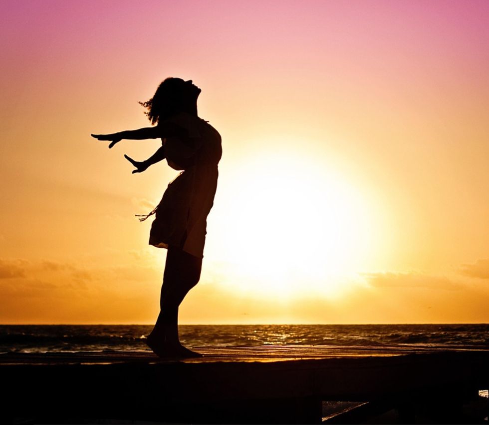 femme qui ouvre ses bras au coucher de soleil en bord de mer